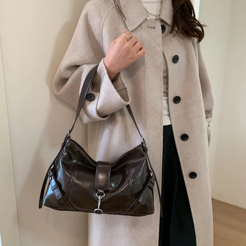 Glossy shoulder bag with central strap and metal clip — brown held by model | BTendance