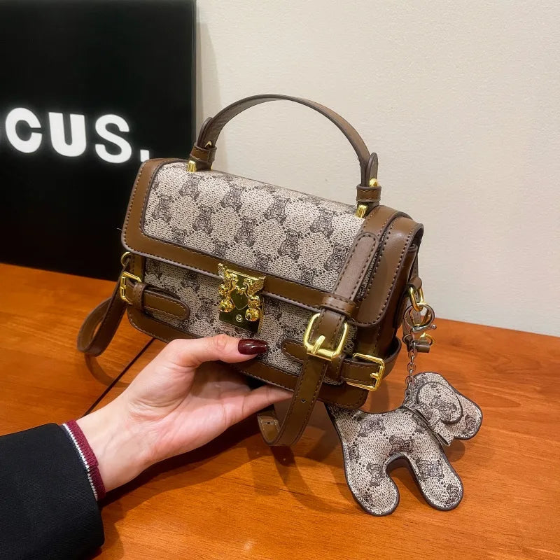 Bear pattern top handle bag with charm – Brown bag held above a wooden table | BTendance