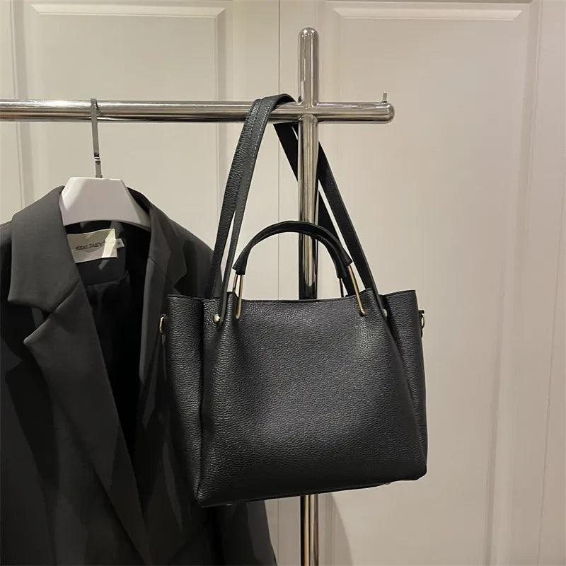 Textured bucket handbag with contrasting dark handles — black hanging on clothing rack | BTendance