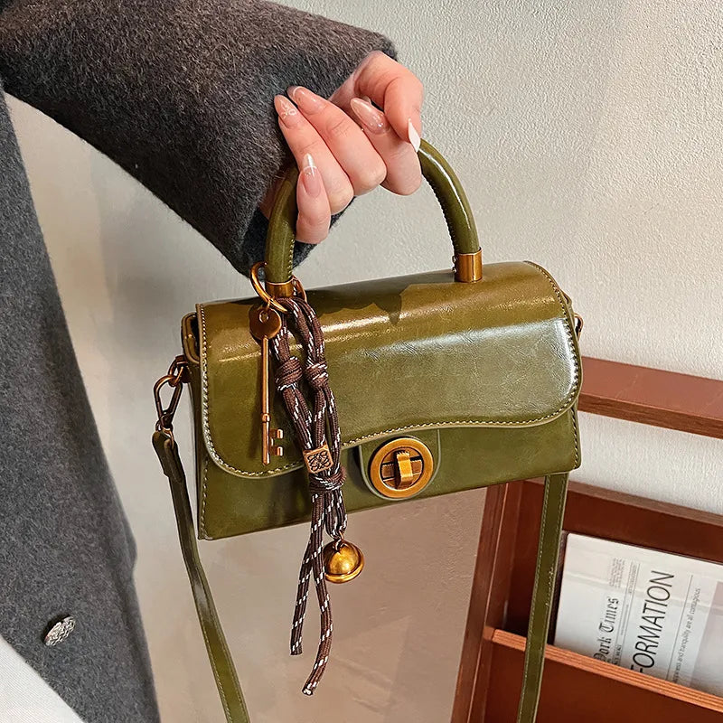 Structured top-handle flap handbag with round gold-tone clasp — green held by handle with scarf accent | BTendance