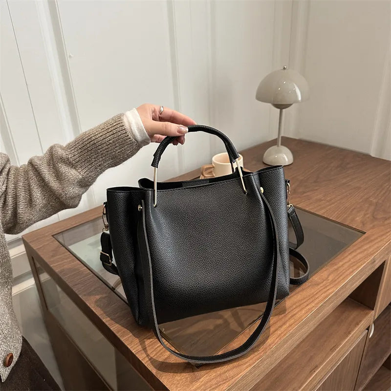 Textured bucket handbag with contrasting dark handles — black held on wooden table | BTendance