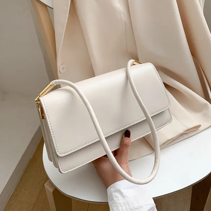Slim rectangular flap shoulder bag with gold-tone strap accents — white held beside cream jacket | BTendance