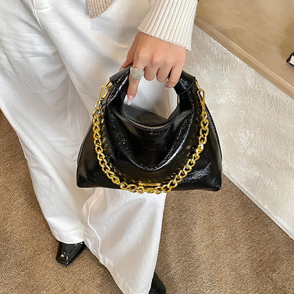 Soft handbag with gold tone chain – Black bag held against a white outfit | BTendance