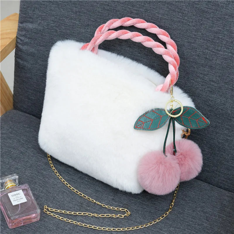 Plush handbag with twisted pink handles and pom-pom cherry charm — white on grey chair | BTendance