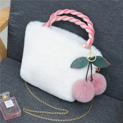 Plush handbag with twisted pink handles and pom-pom cherry charm — white on grey chair | BTendance
