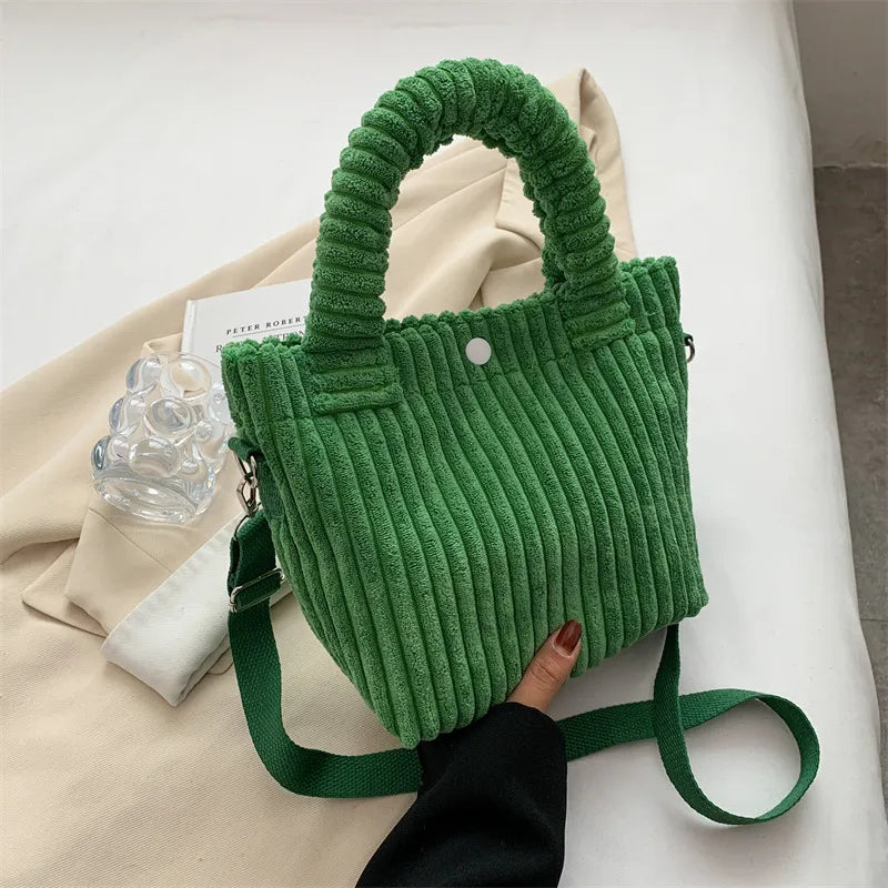 Ribbed plush handbag with rounded handles and long strap — green held above fabric display | BTendance