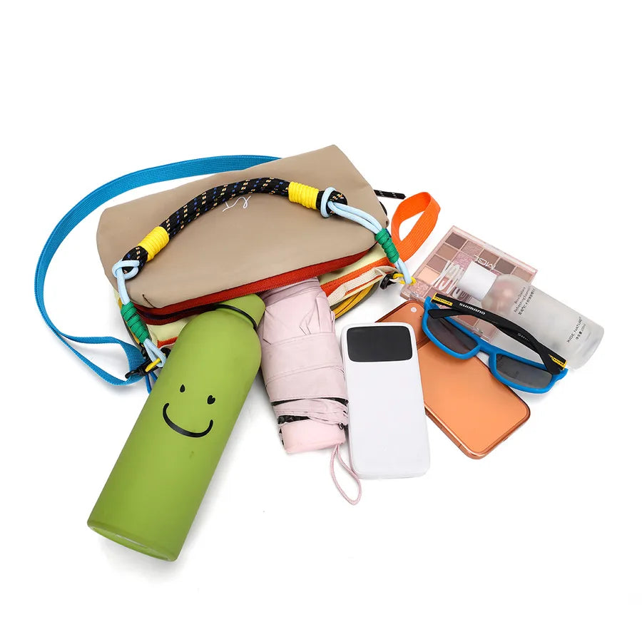 Color-block crossbody bag with rope handle — open bag with personal items arranged beside it | BTendance