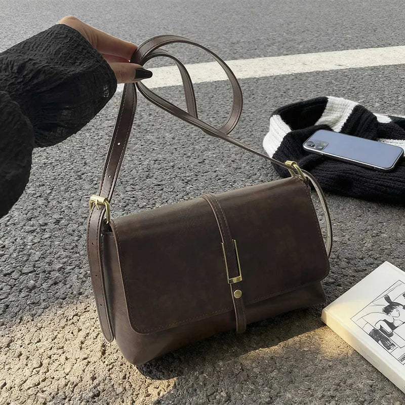 Rectangular flap shoulder bag with slim metal front detail — brown held above table | BTendance