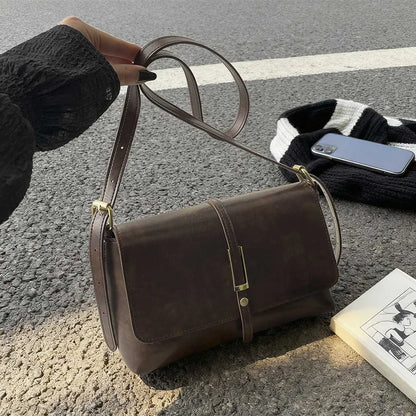Rectangular flap shoulder bag with slim metal front detail — brown held above table | BTendance