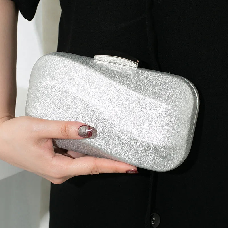 Rounded rectangular evening clutch with metal clasp — silver held against black dress | BTendance