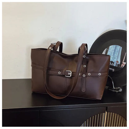 Rectangular shoulder tote with buckle and eyelet detailing — brown on cabinet beside mirror | BTendance