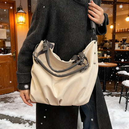 Slouchy nylon shoulder bag with contrasting grey handles — cream carried beside a dark coat | BTendance