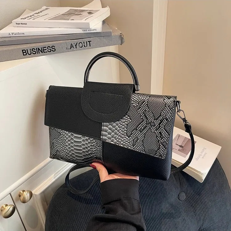 Structured handbag with contrasting reptile-texture panels — black and grey held in one hand | BTendance