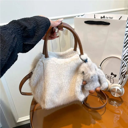Plush top-handle handbag with rabbit charm — white with tan handles held in one hand | BTendance