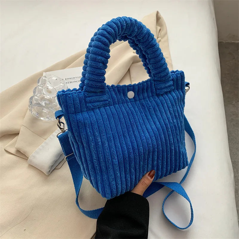 Ribbed plush handbag with rounded handles and long strap — blue held above fabric display | BTendance