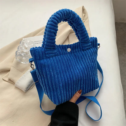 Ribbed plush handbag with rounded handles and long strap — blue held above fabric display | BTendance