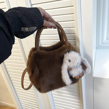 Plush top-handle handbag with rabbit charm — brown held in one hand | BTendance