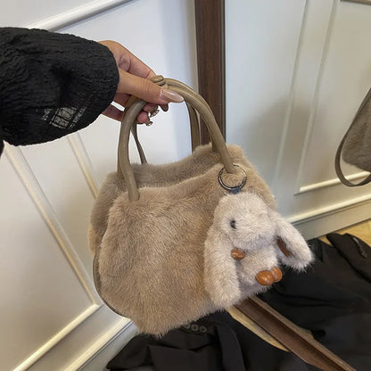Plush top-handle handbag with rabbit charm — taupe held in one hand | BTendance