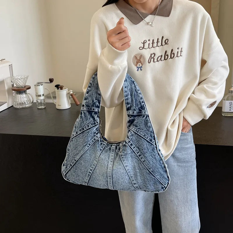 Denim shoulder bag with panel seams – Light blue bag held beside a cream sweatshirt | BTendance