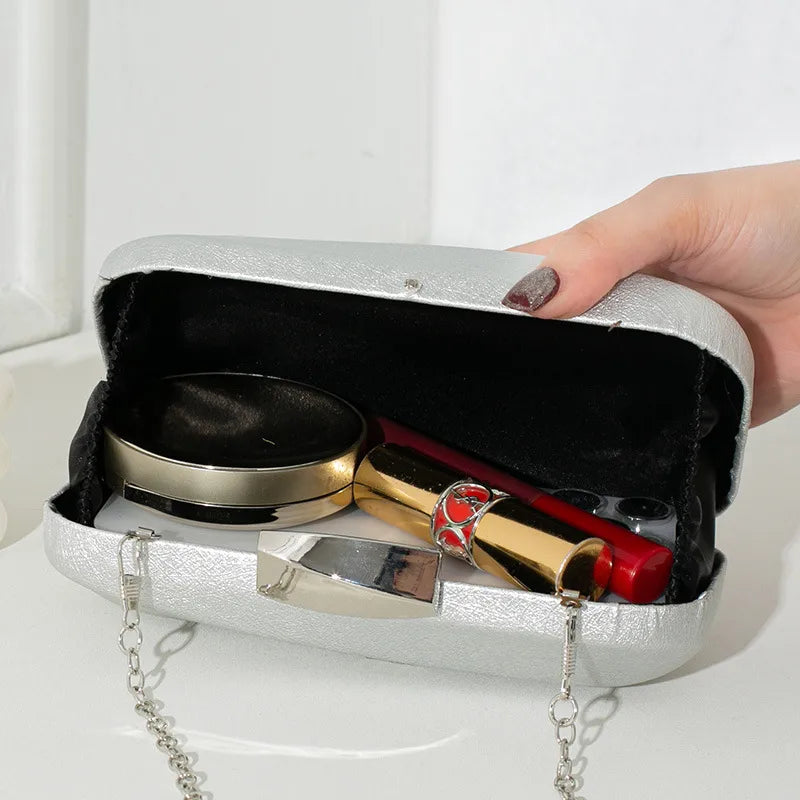 Rounded rectangular evening clutch with metal clasp — silver open with small personal items inside | BTendance
