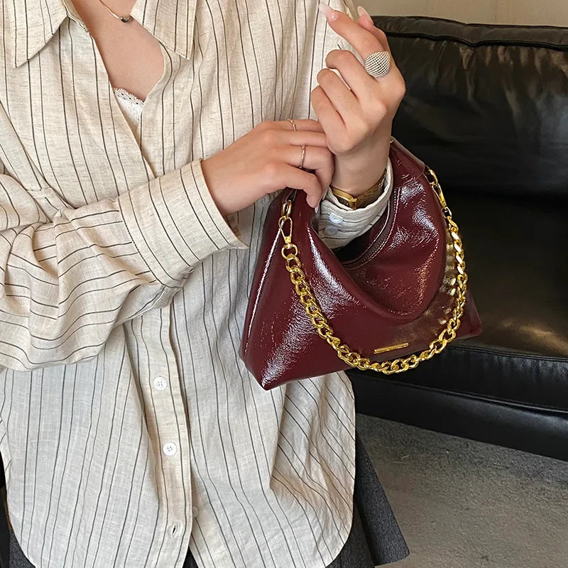 Soft handbag with gold tone chain – Burgundy bag held against a striped shirt | BTendance