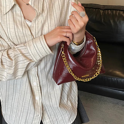 Soft handbag with gold tone chain – Burgundy bag held against a striped shirt | BTendance